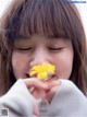 A young girl holding a yellow flower in her mouth.