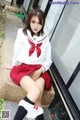 A woman in a school uniform sitting on a stone ledge.