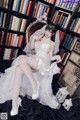 A woman in a wedding dress sitting on a chair in front of a bookcase.