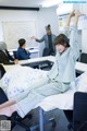 A woman in pajamas stretching on a bed in a classroom.