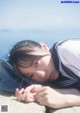 A young woman laying on the ground next to the ocean.