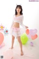 A woman in a white top and pink skirt posing with balloons.